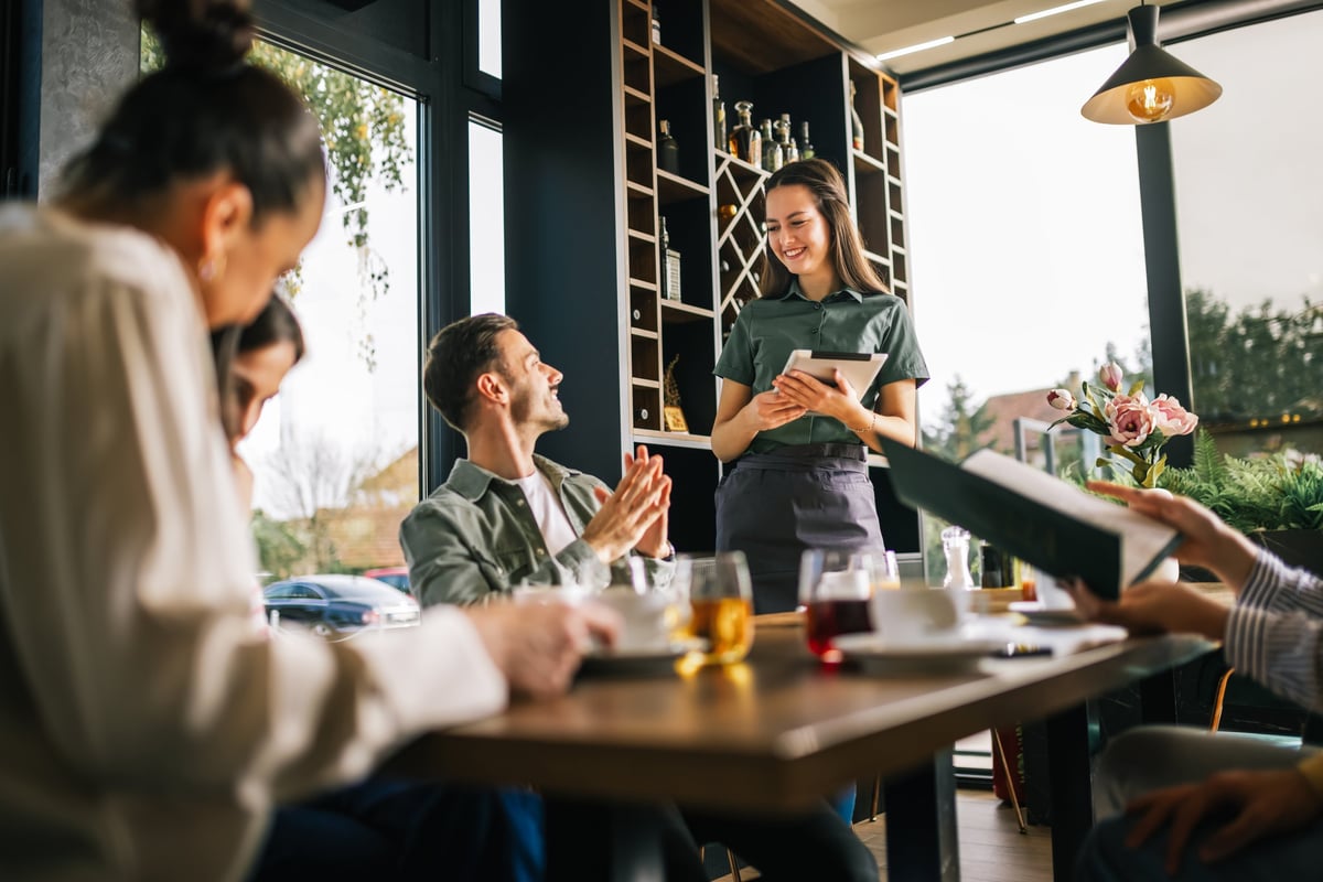 Group of people ordering food from the waitress, waitress writing orders down on tablet