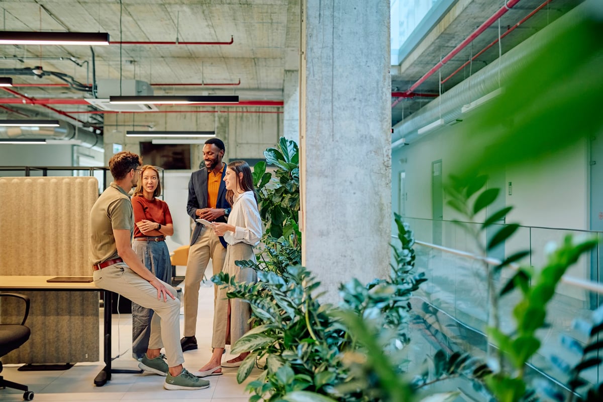 Group of diverse businesspeople engaged in a project discussion within a modern office filled with lush plants
