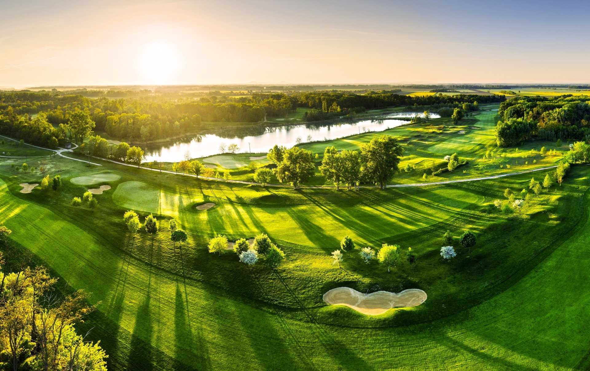 Golf course panorama at dramatic sunrise with green fairways and forest